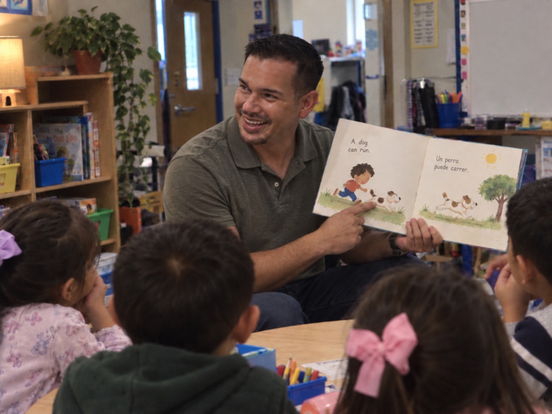 An adult shares a picture book with a group of children
